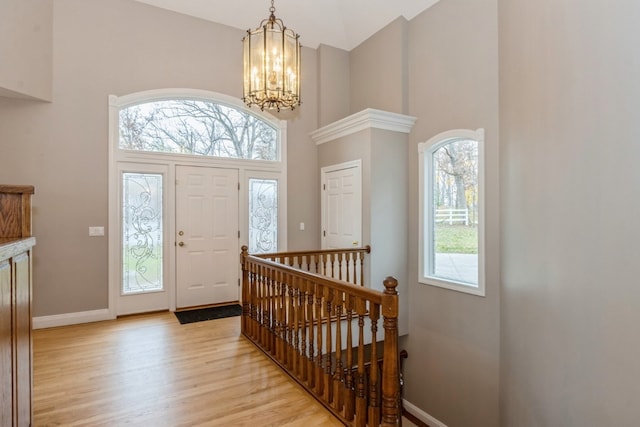 foyer with a towering ceiling, an inviting chandelier, and light wood-type flooring