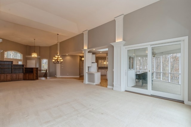 unfurnished living room featuring ornate columns, light carpet, a towering ceiling, and a notable chandelier