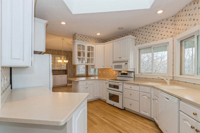 kitchen with white cabinets, white appliances, decorative light fixtures, and a skylight