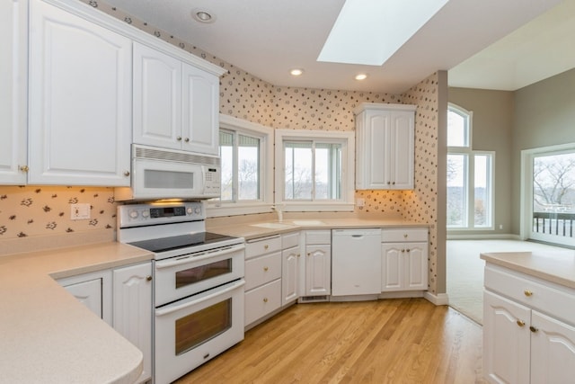 kitchen featuring a skylight, white cabinetry, a healthy amount of sunlight, light hardwood / wood-style floors, and white appliances