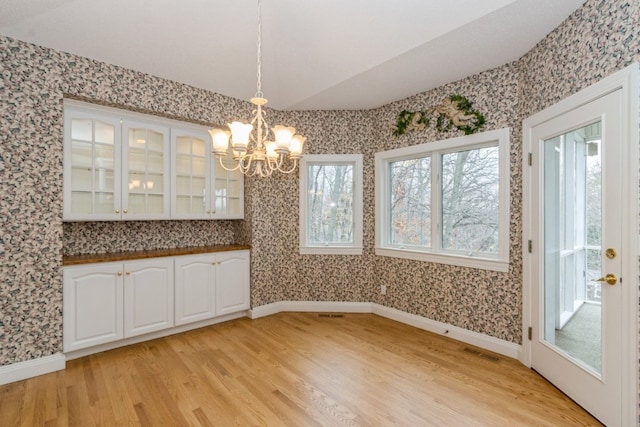 unfurnished dining area with a notable chandelier, light hardwood / wood-style floors, and lofted ceiling