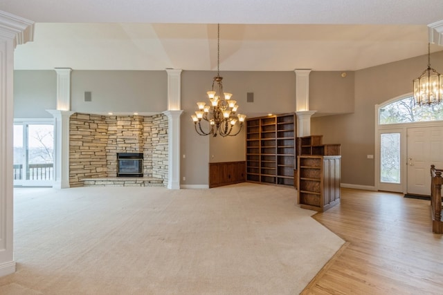 unfurnished living room featuring an inviting chandelier, light hardwood / wood-style flooring, a stone fireplace, and a wealth of natural light