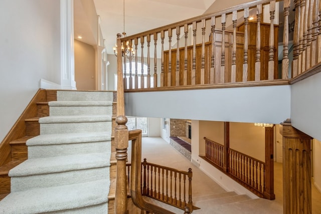 staircase featuring carpet flooring, a high ceiling, an inviting chandelier, and a brick fireplace