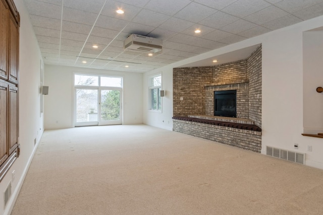 unfurnished living room featuring a fireplace, light colored carpet, and a drop ceiling