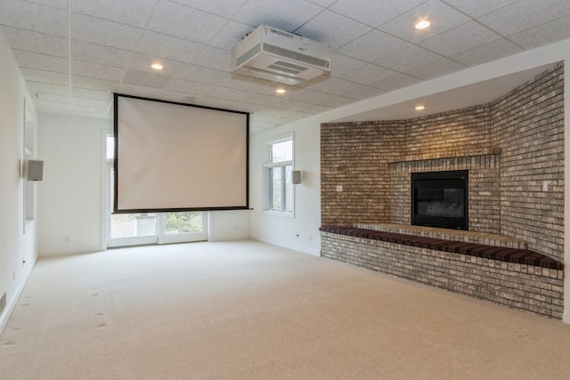 carpeted home theater room featuring a drop ceiling and a brick fireplace