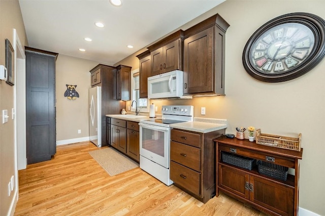 kitchen featuring white appliances, dark brown cabinetry, sink, and light hardwood / wood-style floors