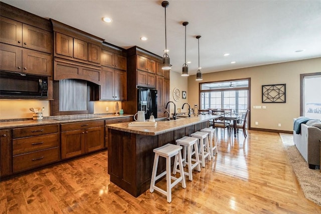 kitchen with a breakfast bar, hanging light fixtures, light wood-type flooring, a center island with sink, and black appliances