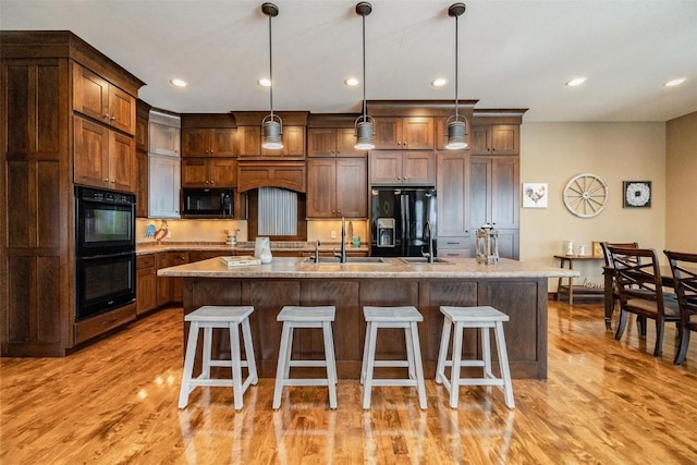 kitchen featuring light stone countertops, hanging light fixtures, black appliances, and an island with sink