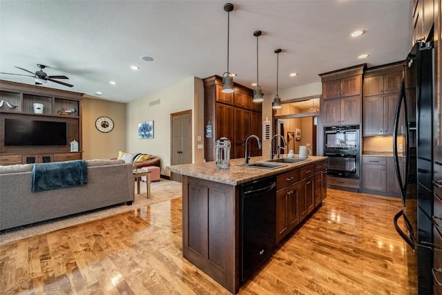 kitchen featuring sink, decorative light fixtures, a center island with sink, light hardwood / wood-style floors, and black appliances