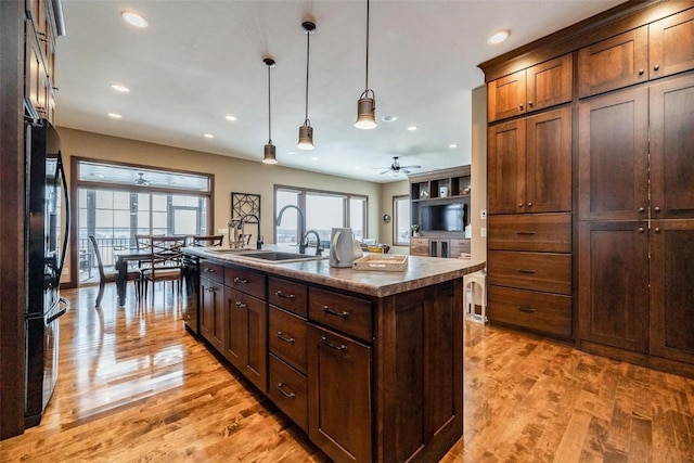 kitchen featuring pendant lighting, sink, a kitchen island with sink, black appliances, and light wood-type flooring