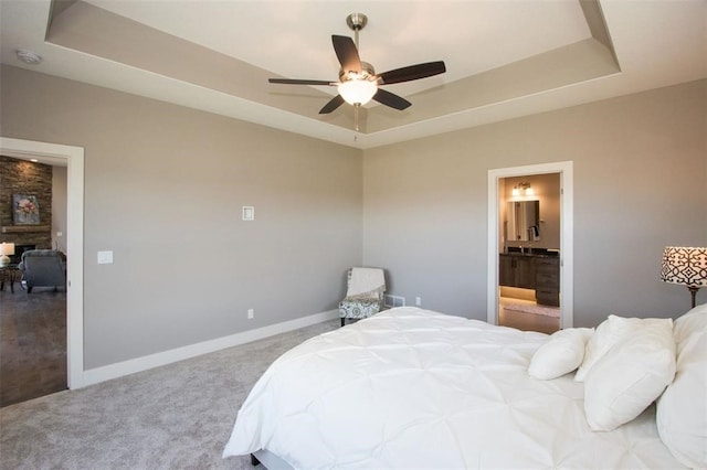 bedroom featuring ensuite bath, ceiling fan, a raised ceiling, carpet floors, and a fireplace