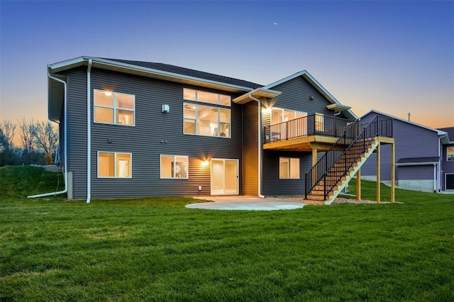 back house at dusk featuring a wooden deck, a patio area, and a lawn