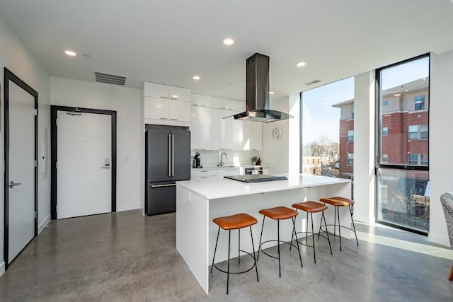 kitchen featuring a kitchen island, stainless steel fridge, island range hood, a breakfast bar, and white cabinets