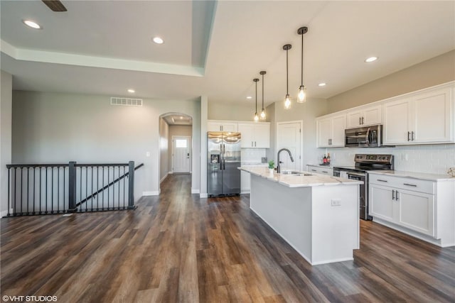 kitchen featuring sink, white cabinets, hanging light fixtures, stainless steel appliances, and a center island with sink