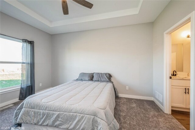 carpeted bedroom featuring connected bathroom, ceiling fan, and a tray ceiling