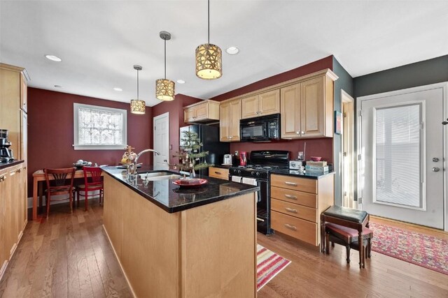 kitchen featuring sink, black appliances, light hardwood / wood-style flooring, hanging light fixtures, and an island with sink