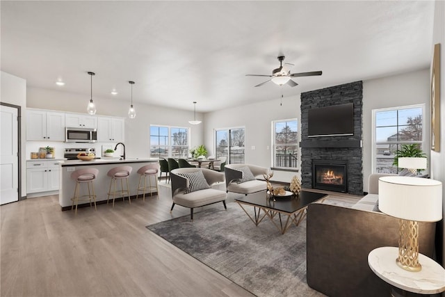 living room with plenty of natural light, light hardwood / wood-style floors, a stone fireplace, and ceiling fan