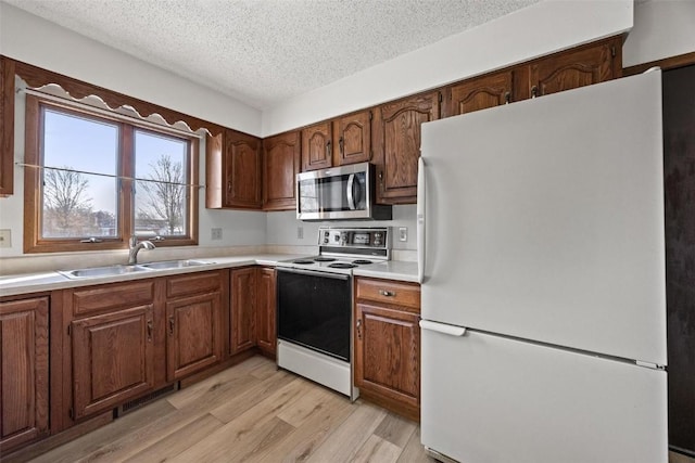 kitchen featuring a textured ceiling, sink, white appliances, and light hardwood / wood-style flooring