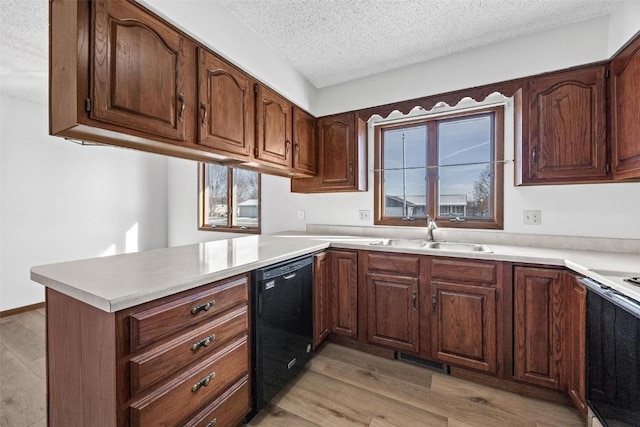 kitchen with kitchen peninsula, a textured ceiling, sink, light hardwood / wood-style flooring, and black dishwasher