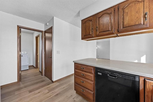 kitchen featuring light wood-type flooring, washer / dryer, black dishwasher, and a textured ceiling