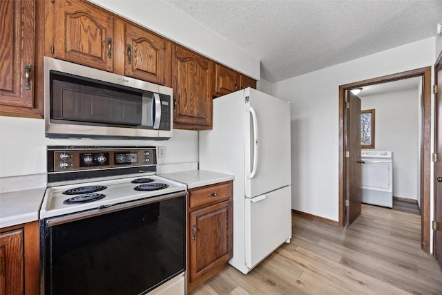 kitchen featuring washer / dryer, white appliances, light hardwood / wood-style floors, and a textured ceiling