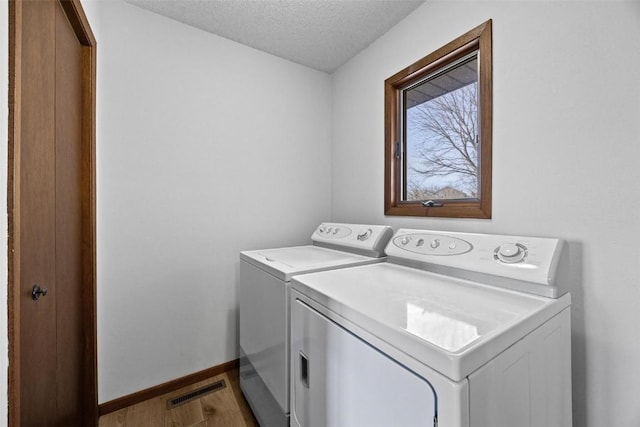 clothes washing area with washing machine and dryer, hardwood / wood-style floors, and a textured ceiling