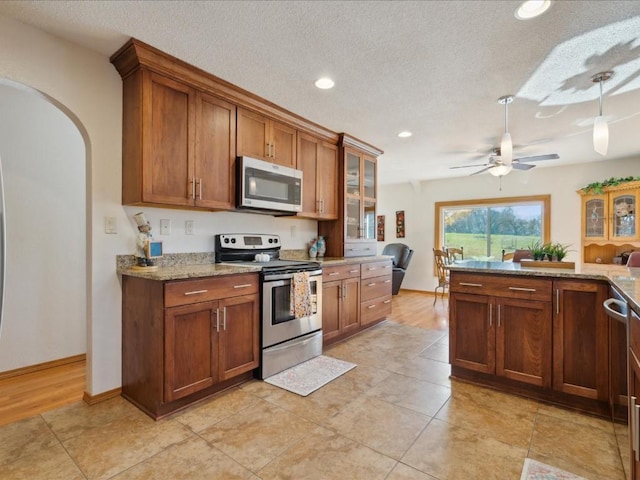 kitchen with ceiling fan, stainless steel appliances, light stone counters, a textured ceiling, and light tile patterned flooring