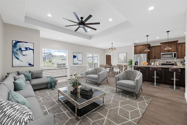 living room with ceiling fan with notable chandelier, sink, dark wood-type flooring, and a tray ceiling