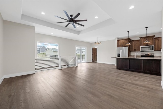 unfurnished living room with ceiling fan with notable chandelier, a tray ceiling, dark wood-type flooring, and sink