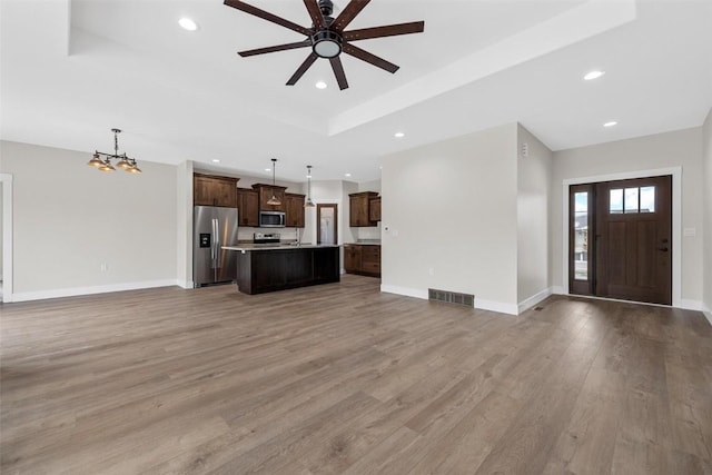 unfurnished living room with a tray ceiling, ceiling fan with notable chandelier, and hardwood / wood-style flooring