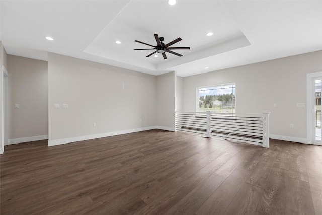 unfurnished living room with a tray ceiling, ceiling fan, and dark wood-type flooring