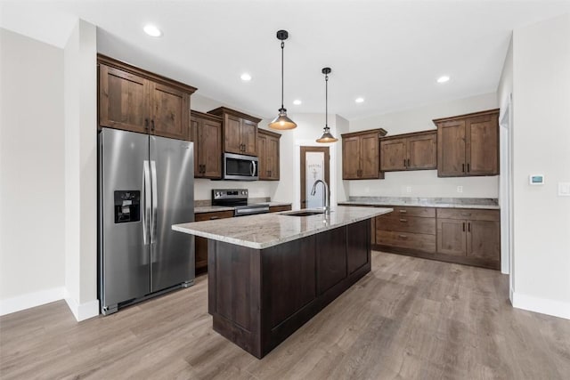 kitchen with sink, light stone counters, light wood-type flooring, and stainless steel appliances