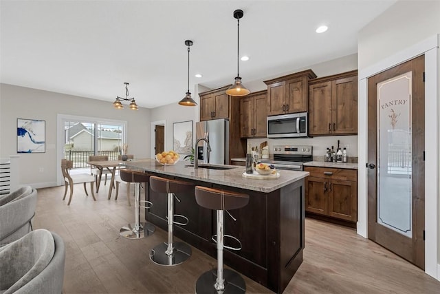 kitchen with hanging light fixtures, a kitchen breakfast bar, light hardwood / wood-style flooring, a kitchen island with sink, and appliances with stainless steel finishes