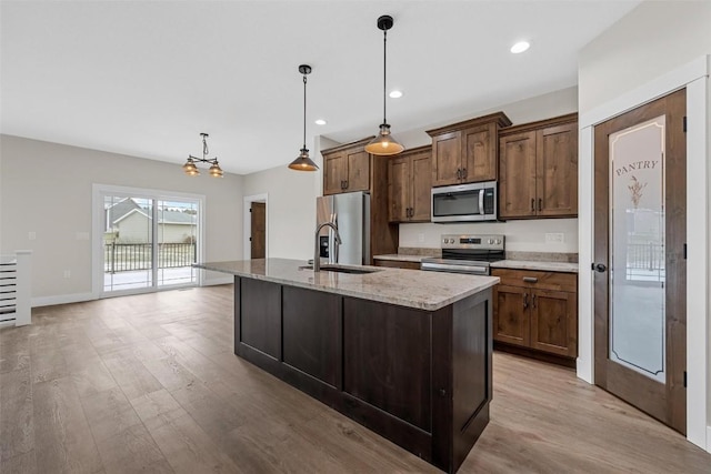 kitchen with decorative light fixtures, stainless steel appliances, light hardwood / wood-style flooring, and a kitchen island with sink