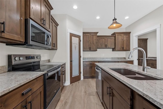 kitchen featuring appliances with stainless steel finishes, light wood-type flooring, light stone counters, sink, and decorative light fixtures