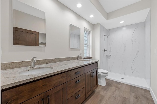 bathroom with tiled shower, vanity, hardwood / wood-style flooring, and toilet