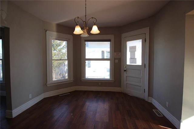 unfurnished dining area featuring dark wood-type flooring and a notable chandelier