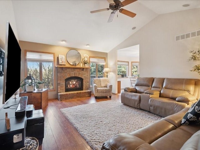 living room featuring a brick fireplace, a wealth of natural light, dark wood-type flooring, and ceiling fan