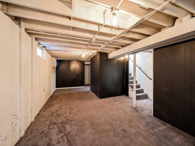 basement featuring dark colored carpet and wood walls