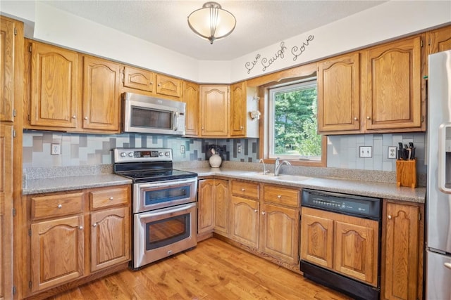 kitchen with light wood-type flooring, stainless steel appliances, tasteful backsplash, and sink