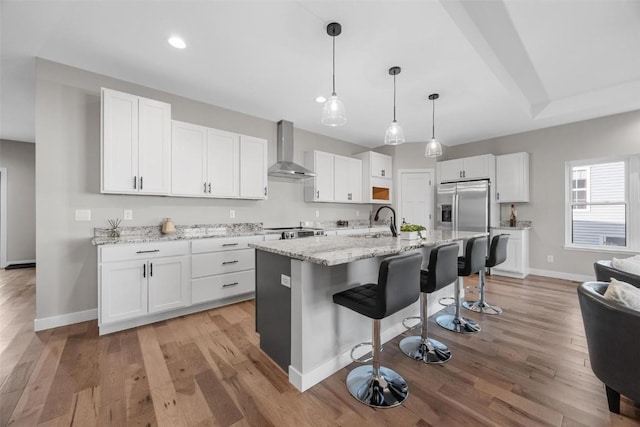 kitchen featuring a center island with sink, white cabinets, light hardwood / wood-style floors, and wall chimney range hood