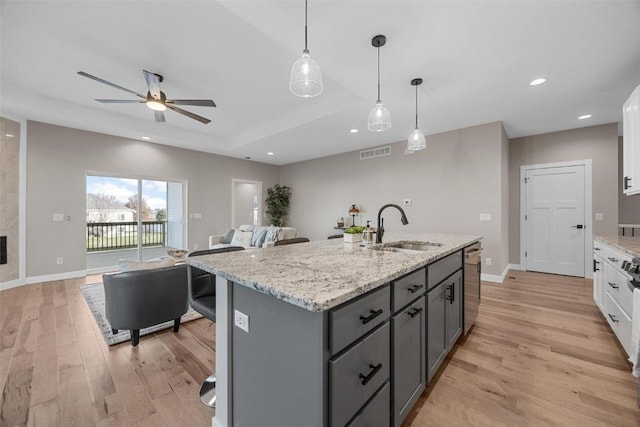 kitchen with pendant lighting, white cabinets, sink, an island with sink, and light hardwood / wood-style floors