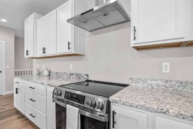 kitchen featuring light stone countertops, wall chimney exhaust hood, stainless steel range with electric stovetop, white cabinets, and light wood-type flooring