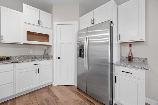 kitchen with white cabinets, stainless steel fridge, light stone counters, and light wood-type flooring