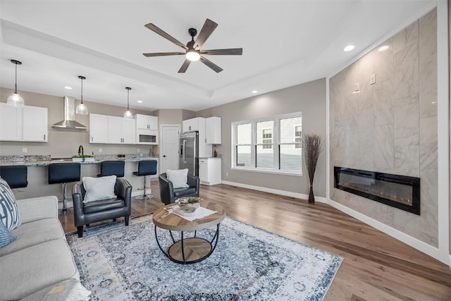 living room featuring a tile fireplace, ceiling fan, and light wood-type flooring