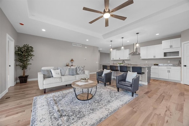 living room with a tray ceiling, ceiling fan, and light hardwood / wood-style flooring