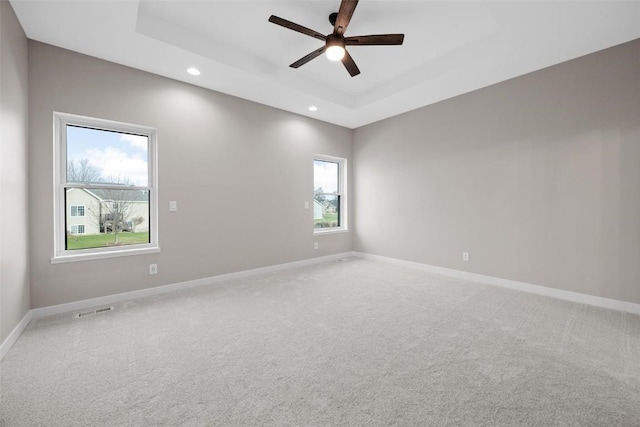 carpeted spare room featuring a raised ceiling, ceiling fan, and plenty of natural light