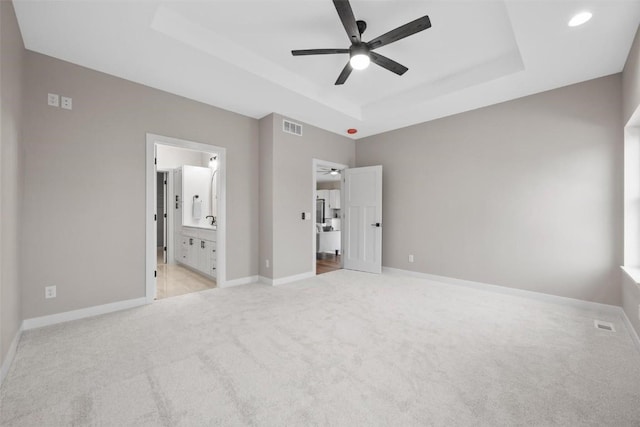 unfurnished bedroom with ensuite bathroom, a raised ceiling, ceiling fan, and light colored carpet