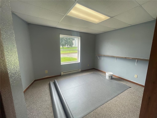 carpeted spare room featuring a drop ceiling and a baseboard heating unit