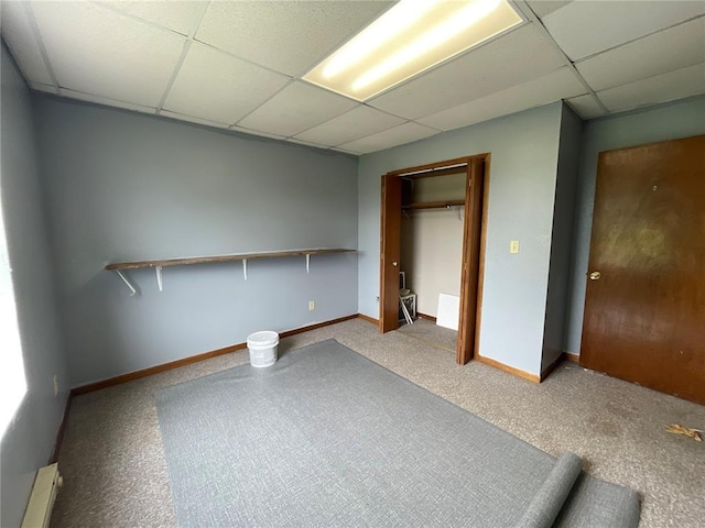 unfurnished bedroom with a paneled ceiling, light carpet, a closet, and a baseboard heating unit